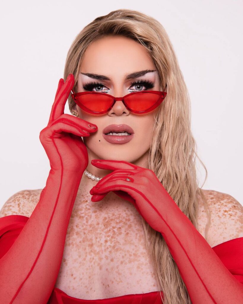 Drag Race UK star Elektra Fence poses with red gloves near her face with matching red glasses