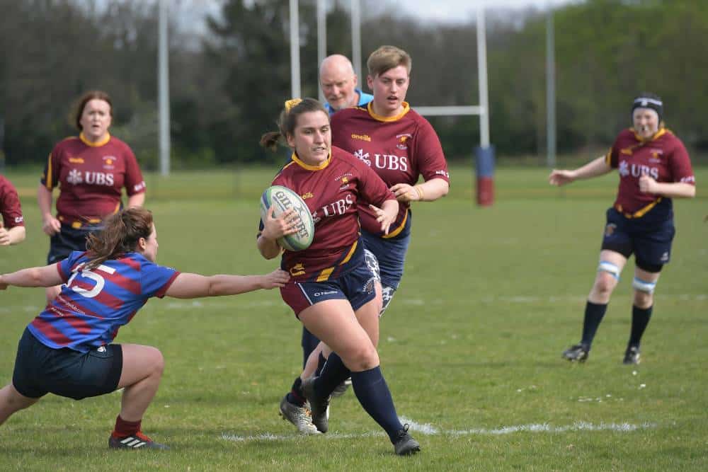 Alix Fitzgerald is seen in the top left corner of the picture wearing a red rugby jersey as she runs behind her teammates